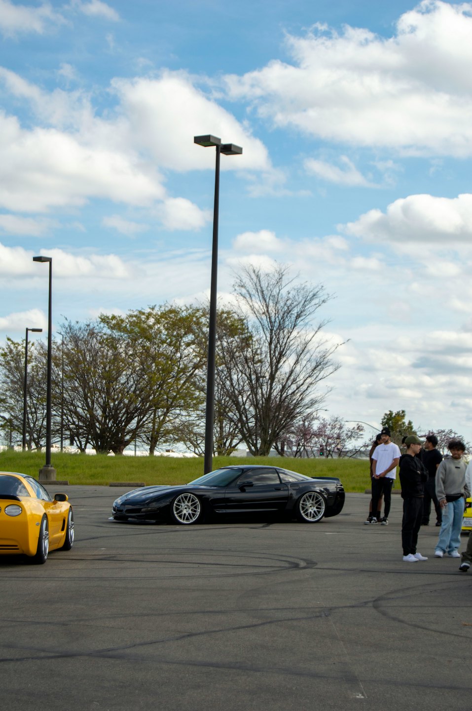 Car enthusiasts admire modified sports cars in a parking lot.