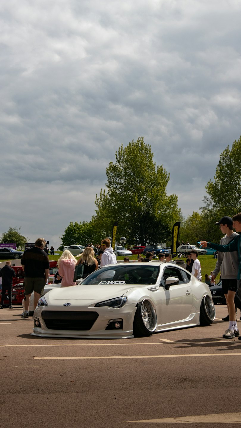 People admire a customized white sports car at an outdoor event.