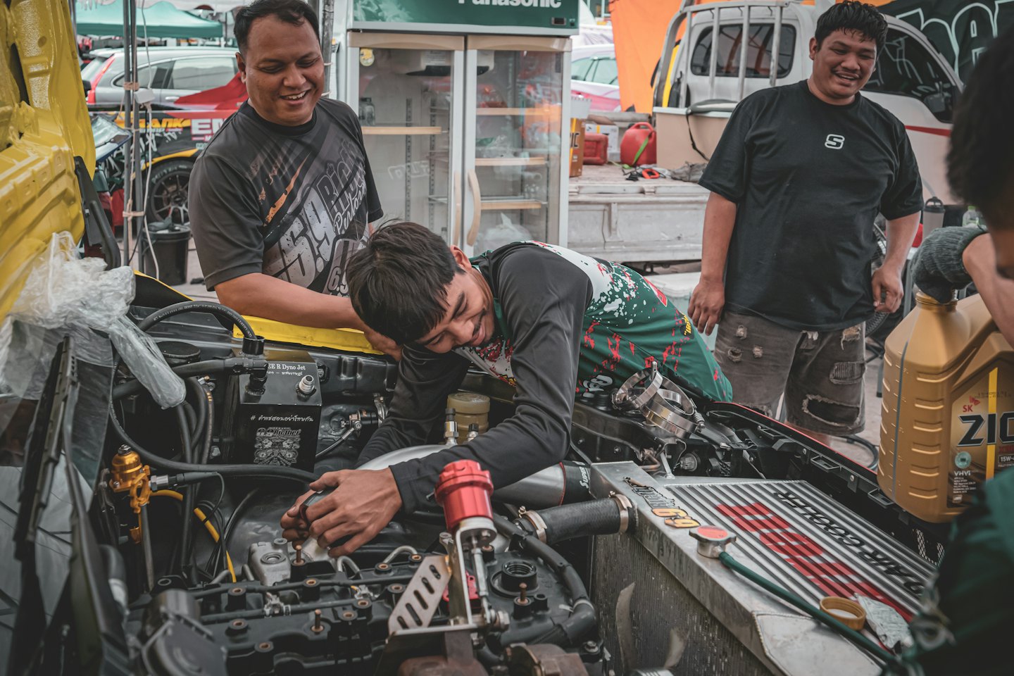 Three men working together on a car engine outdoors.